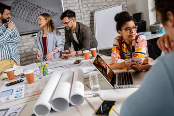 Group of young business people in casual wear discussing architectural designs while sitting in the creative office.