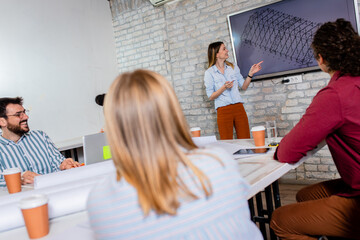 Group of young business people in casual wear discussing architectural designs while sitting in the creative office.