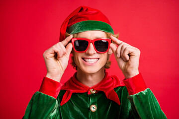 Portrait of positive fairy elf guy touch his modern x-mas specs isolated over red bright color...