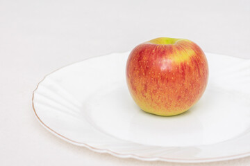A ripe red Apple on a white plate, closeup, side view
