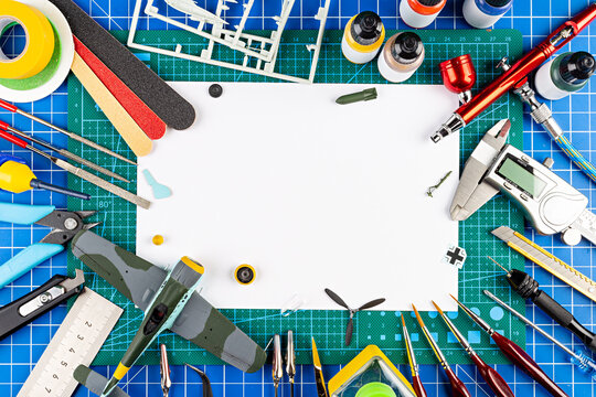 desktop view from above of assembly painting of retro scale model plane concept copy space background. modeling tools airbrush gun paint kit parts blue green cutting mat knife and brush work desk