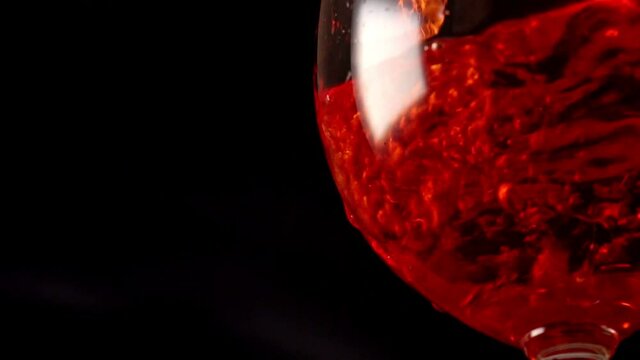 Aperol spritz pouring to the glass on black background.
