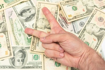Man shows sign peace with fingers, dollar bills in the background, male hand, close-up