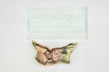 Crumpled five-dollar bills and medical mask, white background, copy space
