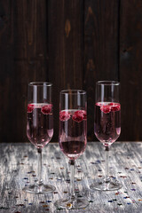 Pink sparkling cocktail with a raspberry. Glass of champagne and glitter stars on wooden table