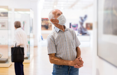 mature European man examines paintings in an exhibition in hall of an art museum
