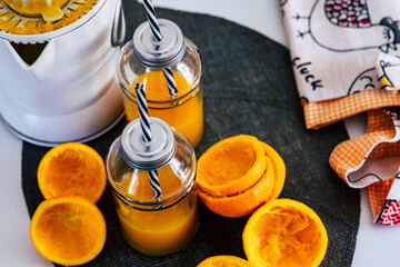 Electric squeezer and cut oranges, two glasses on the table with orange juice and straw