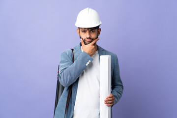 Young architect Moroccan man with helmet and holding blueprints over isolated background thinking