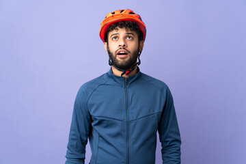 Young Moroccan cyclist man isolated on purple background looking up and with surprised expression