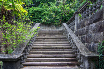 Ancient staircase are grey stone with stone balusters on a background of green vegetation