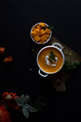 Vegetarian autumn pumpkin cream soup with seeds in white bowls on a dark background.  The concept...