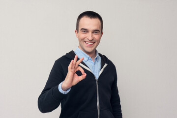 Portrait young handsome man, giving OK sign with fingers, white background. Positive people emotion facial expressions, symbol