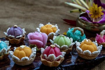 A variety of elegantly beautiful Thai Desserts (Khanom Wan Thai) colorful variations serving in a dark wooden, The bites in gold color and different flower shapes, Thai dessert, Auspicious dessert.