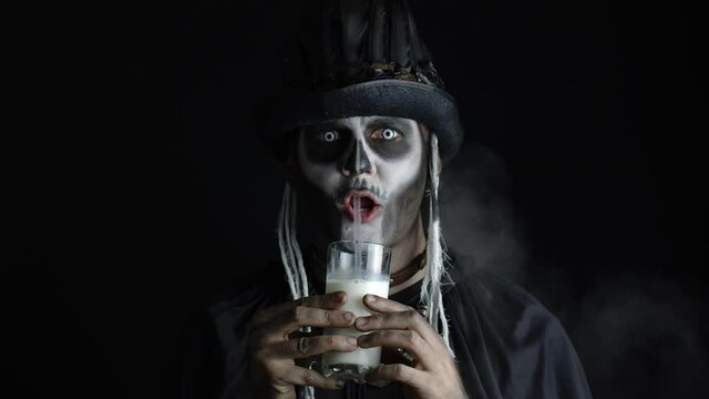 Creepy man with skeleton makeup in top-hat. Guy looking at camera, drinks milk from a glass
