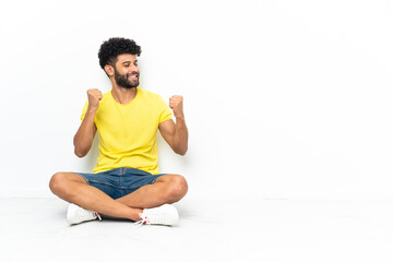 Fototapeta premium Young Moroccan handsome man sitting on the floor over isolated background celebrating a victory