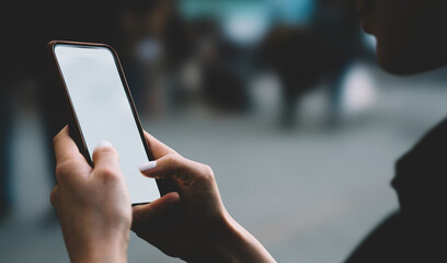 Crop anonymous young woman with smartphone downloading chosen application in open air