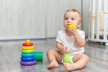 A baby is playing on the floor. The boy is sitting on the floor. The child takes the toy into his mouth and licks it.