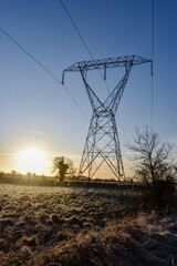 Electricity Pylon in Frozen Meadow at Sunrise
