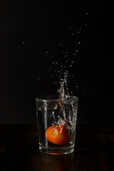 Tomato splashed in the clear water glass with water splashing in all directions on the table isolated on black background