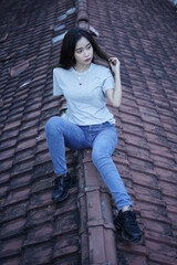 The blonde girl sits on the roof tile while stylishly wearing a gray shirt. female t-shirt models for mockups and templates.