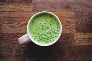 A cup of matcha latte on a wooden table in a cafe.