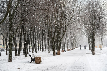 The first snow falls on a Park bench. Snow storm, snowstorm in the city. The first snow on a dark path and footprints on it. Heavy snowfall in the Park, large snowflakes fall on the sidewalk.