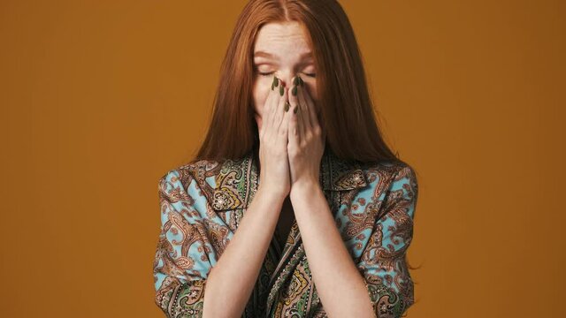 An attractive young woman is sneezing standing isolated over brown background
