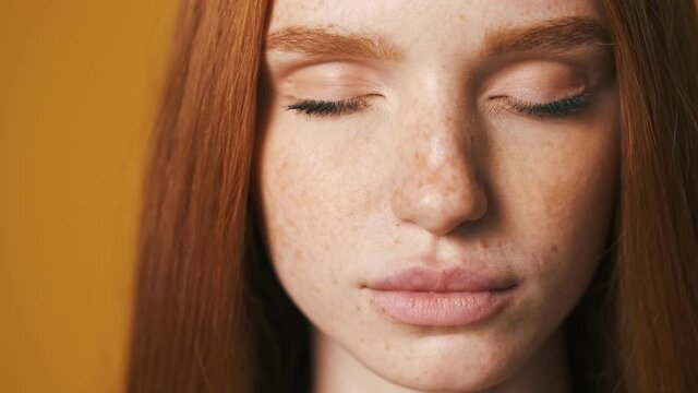 A close-up view of a calm young woman is opening her eyes and looking to the camera isolated over brown background