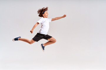 Children engaged in sport. Full-length shot of a teenage boy jumping isolated over grey background, studio shot