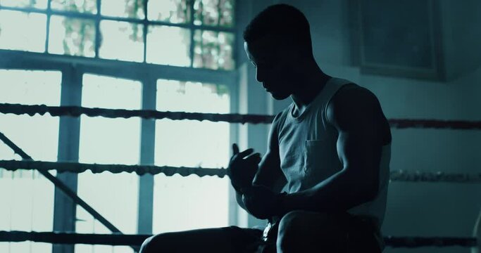 Cinematic slow motion shot of a professional young muscular african man is wrapping black bandages before to start practicing shadow boxing work out in a ring. 
