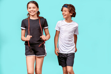 Obraz premium Good workout. Two happy teenagers, boy and girl with jumping rope looking away and smiling while standing isolated over blue background