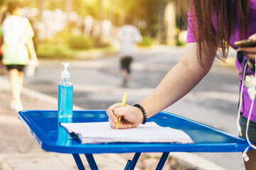 Blue alcohol gel bottle and a register book on the table for athletes to prevent Corona Virus (COVID -19) infection and spread before exercising in public park. New normal lifestyle. Selective focus