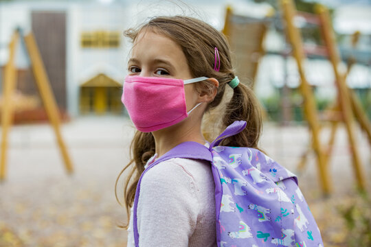 Schoolgirl wearing protective fabric reusable face mask going to school. School education during the coronavirus pandemic. Security measures and social distancing