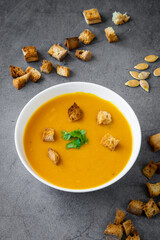 Pumpkin soup with coriander and gluten free croutons in a white bowl with croutons and pumpkin seeds in the background. Seasonal autumn / winter food, healthy and fresh