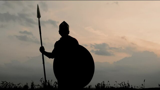 Silhouette of man in armour posing with spear in field.