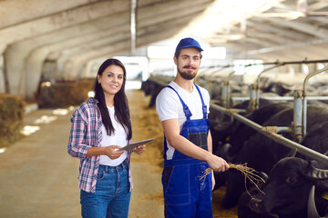 Dairy farm workers standing in cowshed near row of stables looking at camera and smiling