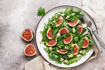 Fresh diet salad figs, arugula and blue cheese in a plate on a rustic beige background. Vegan and vegetarian lunch or dinner. Top view, flat lay, copy space.