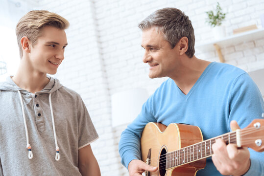 Father is playing on guitar and son is listening.