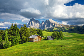 Fototapeta na wymiar Famous Alpe di Siusi - Seiser Alm with Sassolungo - Langkofel mountain group in background at sunset. Wooden chalets in Dolomites, Trentino Alto Adige region, South Tyrol, Italy