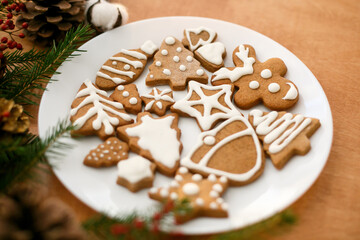 Christmas gingerbread cookies on white plate on wooden background with fir branches