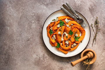 Baked pumpkin slices with herbs and cheese in a plate on a beige rustic background. Top view, flat lay, copy space.