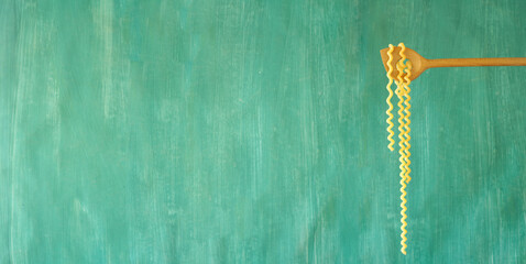 italian fusili spaghetti pasta hanging on a wooden spoon against green background