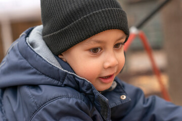 A little smiling boy in a blue jacket and black hat walking in the park