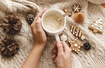 Hands holding warm coffee on background of cozy knitted sweater with christmas gingerbread cookies