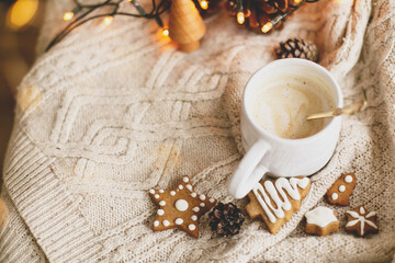 Warm coffee on background of cozy knitted sweater, christmas gingerbread cookies, lights