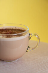 mug of coffee with milk sprinkled with chocolate chips, and foam, on yellow background. Energy and cheerfulness in morning.