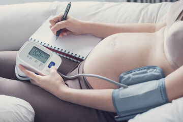 Pregnant woman measuring blood pressure at home, health check of expecting mom