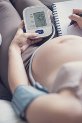 Pregnant woman measuring blood pressure at home, health check of expecting mom