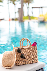 Weaving bag and hat with sunglasses and sunscreen lotion next to a swimming pool, summer travel concept