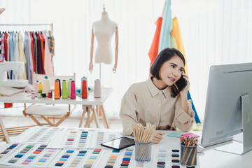 Asian woman designer, talking on the phone with the customer and taking note of the work details.
